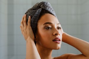 A Black woman holds a gray towel wrapped around her hair