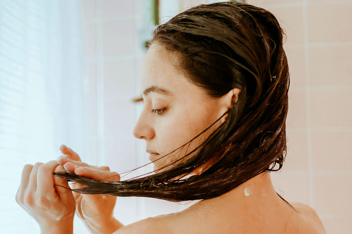 A woman, seen from the neck up, looks at her wet hair in the shower.