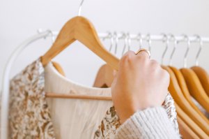 A hand lifts a printed top on a hanger from a rack of clothing.