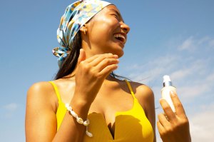 A woman in a yellow swimsuit holds a bottle of sunscreen while smiling