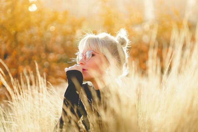 blonde woman wearing glasses sitting in a field 