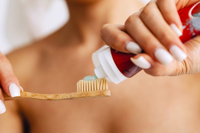 wooden toothbrush with toothpaste being applied to it 