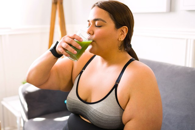 woman in a sports bra drinking a green juice 