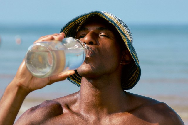 black man wearing hat drinking water at the beach