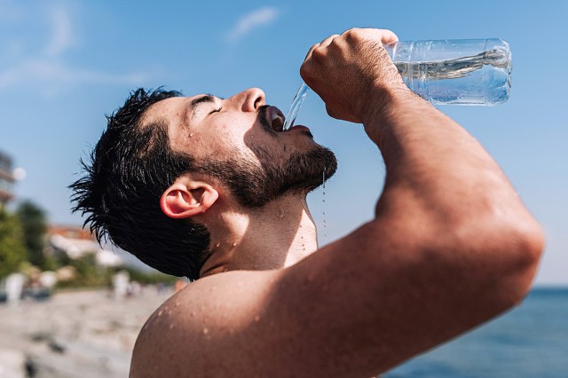 white man drinking water out of a bottle at the beach