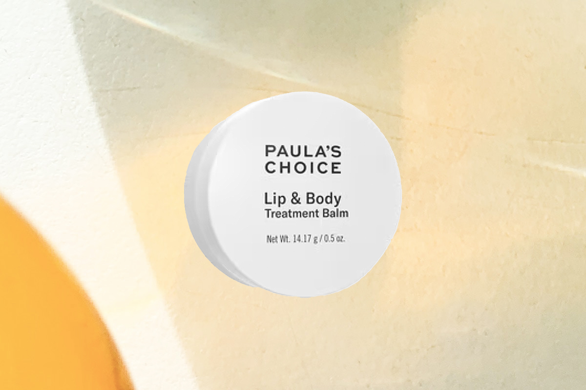 A small container of Paula's Choice Lip & Body Treatment Balm against a warm-toned abstract background.
