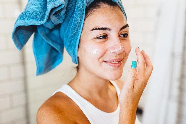 woman with a towel on her head applying skin care to her face