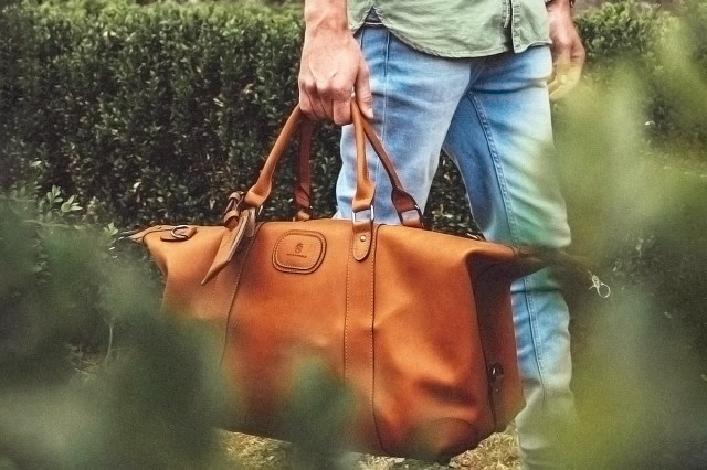 man holding duffle bag near grass