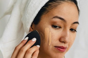 asian woman applying foundation with a black sponge
