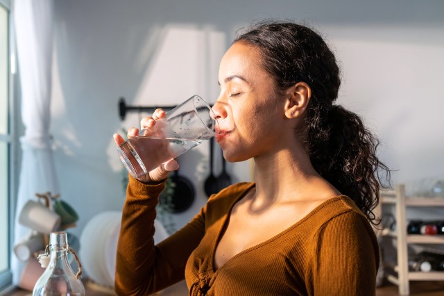 Young beautiful Latino woman holding clean water into glass in kitchen.