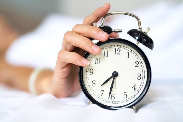 Close up hand of woman touching alarm clock at bedroom at home.