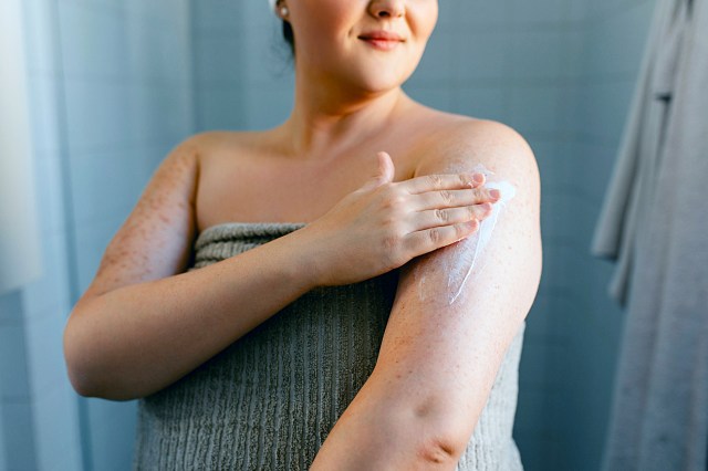 Plus sized woman in a towel in the bathroom putting lotion on her arm