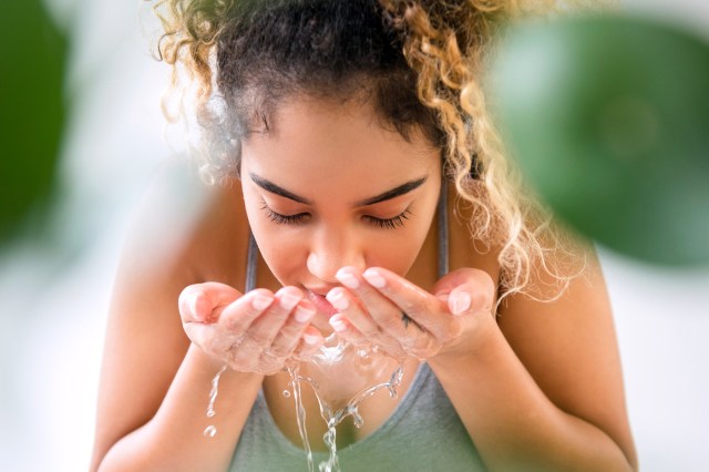Mixed Race woman splashing water on face 