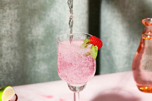 a pink drink being poured into a wine glass