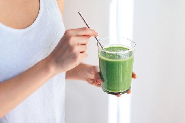 Cropped shot of young woman drinking vegan smoothie with metal straw.