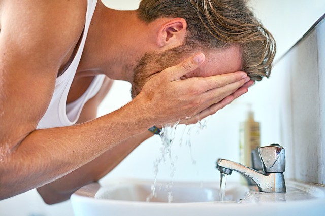Blonde man washing his face with water in sink