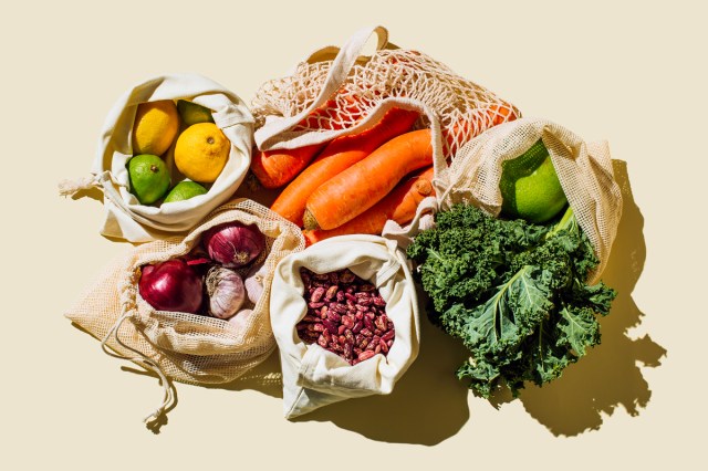 Variety Fresh of organic fruits and vegetables and healthy vegan meal ingredients in reusable eco cotton bags on beige background .