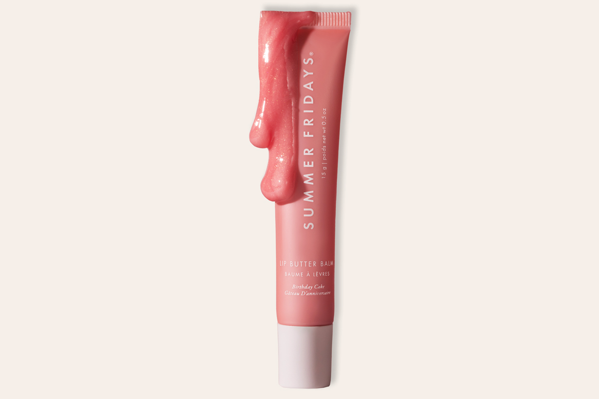 A tube of Summer Fridays Lip Butter Balm in a pink shade, with gloss dripping over the top