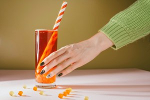 a woman's hand reaching for an orange drink in a tall glass
