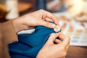 hands and sewing clothes button in studio for designer wear, fashion garment and creative fabric design