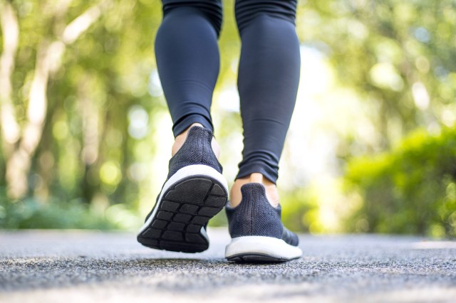 Cropped image of person walking, jogging, on road. Black leggings and black sneakers