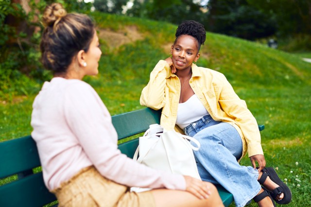 Two female friends sitting on a park bench talking