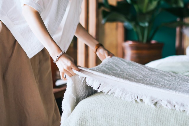 Woman making bed, placing white blanket on the made bed