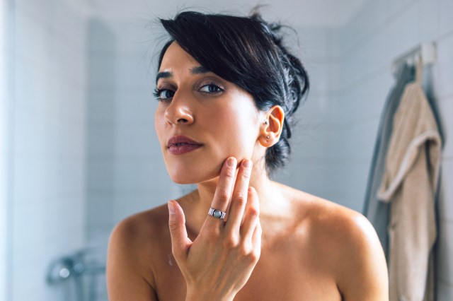Woman touching her face, looking at her skin in a bathroom mirror