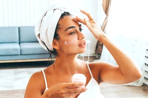 Woman with towel on her head applying skin care product to her face