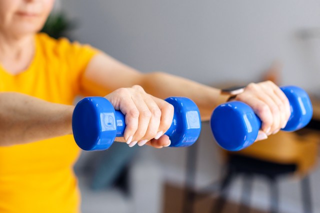 Close-up of woman in yellow t-shirt lifting small blue weights