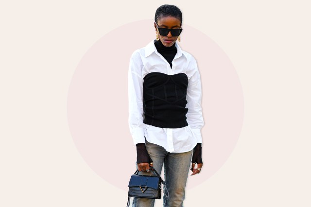  A guest wears black sunglasses, gold pendant earrings, a black wool ribbed turtleneck pullover, a white shirt, a black corset, blue and yellow faded denim cigarette pants,