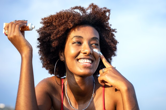 Woman smiling, putting sunscreen on her face, on her cheek