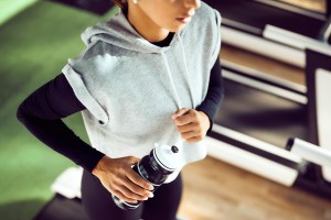 Cropped image of a woman running on a treadmill, holding a water bottle