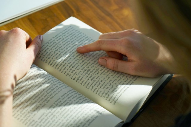 Close-up of person reading book, finger pointing to words