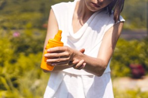 Woman putting sunscreen on her arms, holding orange sunscreen bottle