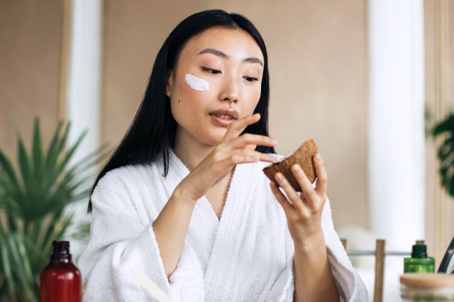 Woman putting facial cream on her face, in a bathrobe