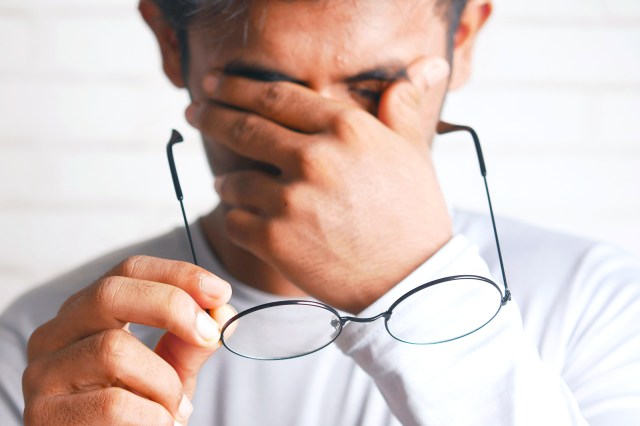 Man rubbing his eyes holding glasses