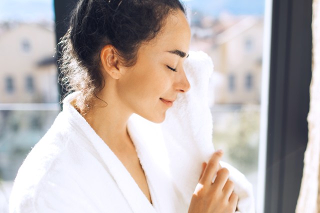 Pretty woman cleaning her face in morning with white towel in bathroom