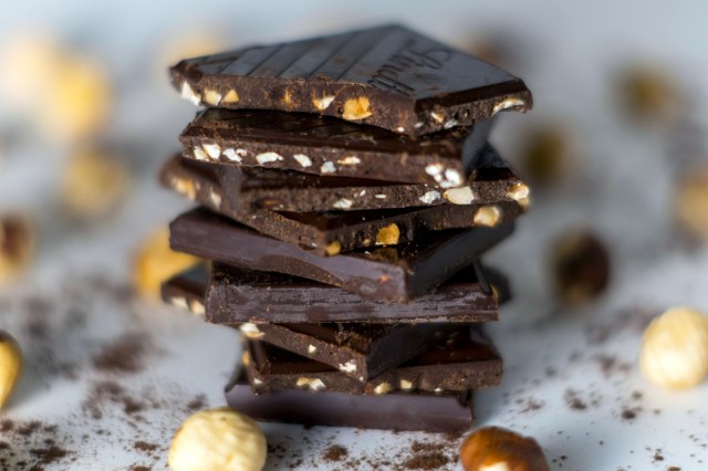 Close up image of stacked dark chocolate with nuts inside and nuts around