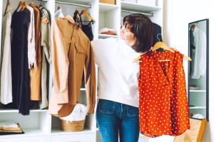 Woman looking at 2 pieces of clothing in closet, choosing what to wear