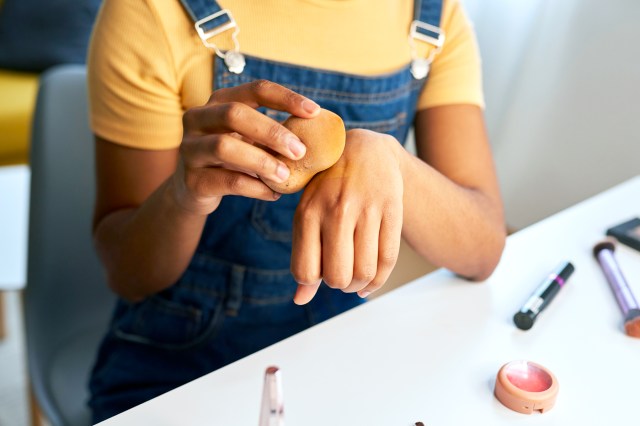 Woman wearing overalls using make-up sponge, blotting something on her hand