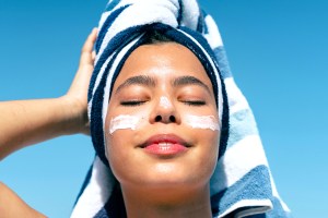 Woman with towel on her head and sunscreen on her face with her eyes closed