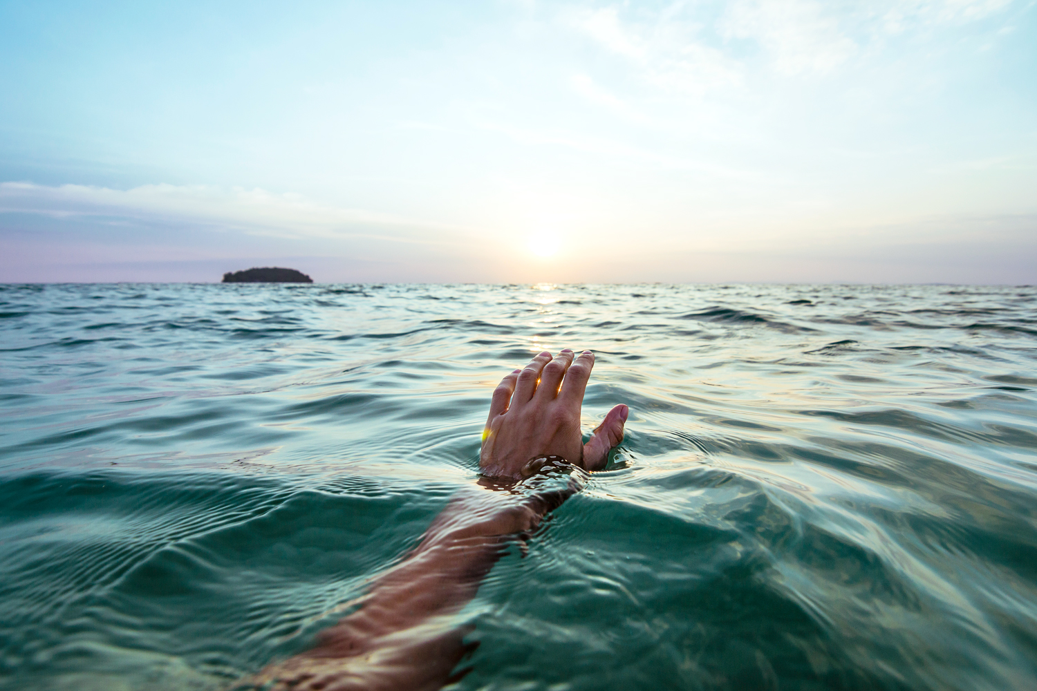 Person's hand emerges from calm water, lagoon sunrise