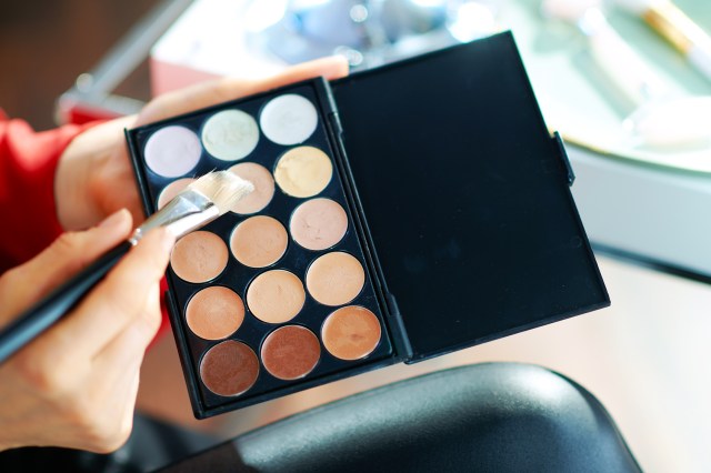 Woman holding brush, using concealer palette