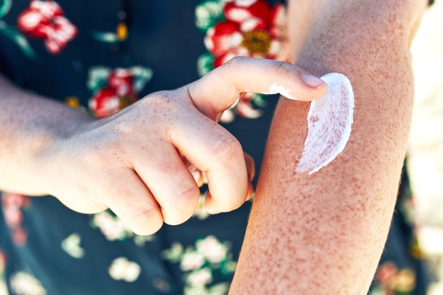 Cropped image of a person applying sunscreen to freckled arm