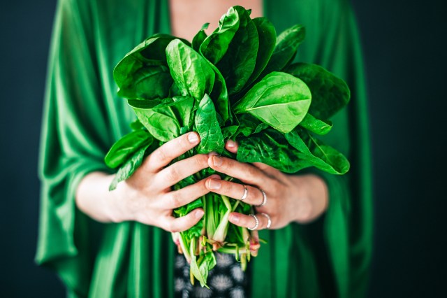 Close up of woman holding spinach in her hands, wearing a green shirt