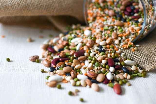 Various/mixed beans, seeds, and legumes spilled out of a glass container