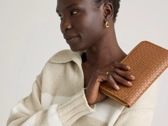 Woman holding Quince handwoven leather wallet next to her face.