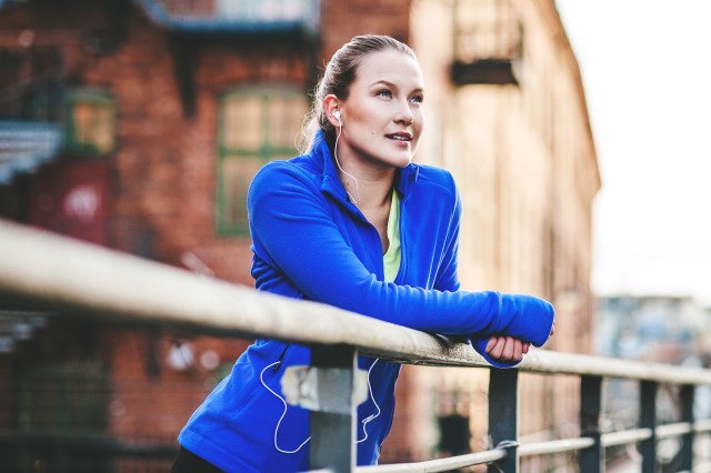 Athletic woman leaning over railing looking up, headphones in her ears