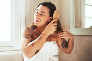 Woman brushing her hair in the bathroom, wearing a towel